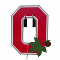 A large red and white cutout letter 'O' mounted on a black metal fence, with a green maple leaf decoration hanging in front. A street scene with parked cars and buildings is visible behind the sign.
