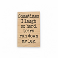 A rectangular light wood sign with black engraved text that reads, 'Sometimes I laugh so hard, tears run down my leg.' The sign is photographed against a dark background.